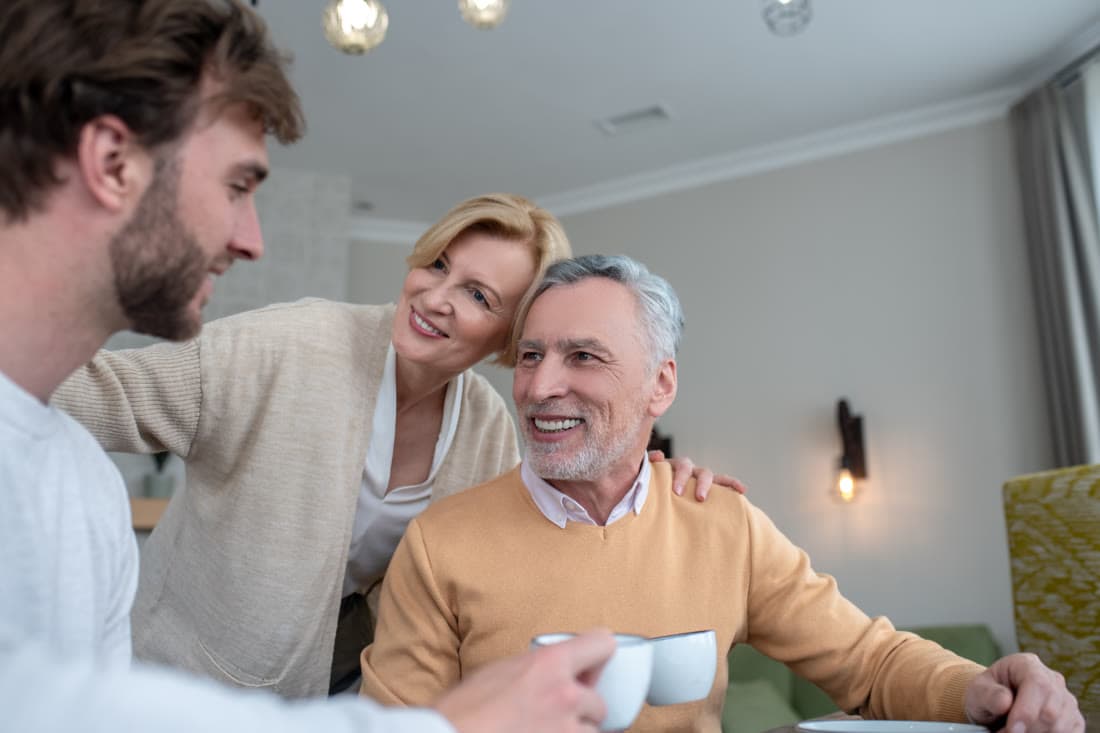 A grown son sitting over coffee with his mother and father at a kitchen table