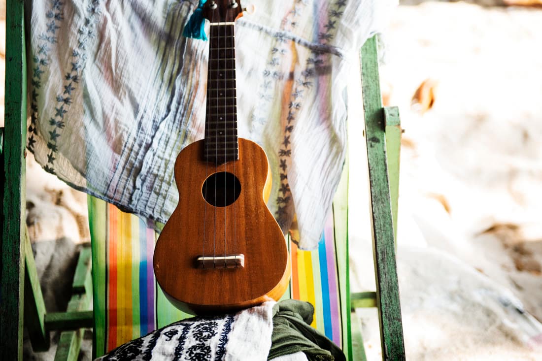 A ukulele resting on a striped deckchair on the sand
